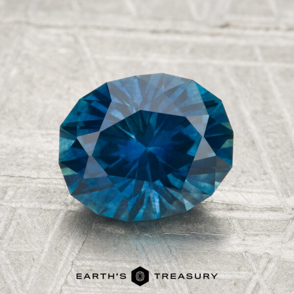 2.30-Carat Montana Sapphire (Heated) A 2.30-carat heated Montana sapphire, oval and blue, is displayed on a textured gray surface with "Earth's Treasury" written below.