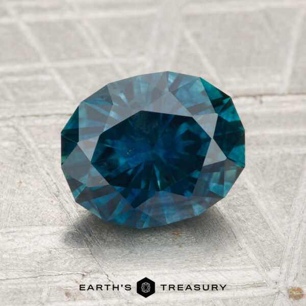 2.17-Carat Montana Sapphire (Heated) A 2.17-carat heated Montana sapphire rests on a light textured surface, with "EARTH'S TREASURY" and a hexagon logo displayed beneath it.