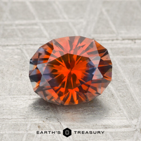 2.08-Carat Montana Sapphire (Heated) A 2.08-carat oval-cut Montana sapphire (heated) with deep orange and brown hues rests on a textured metallic surface; "EARTH'S TREASURY" appears below.