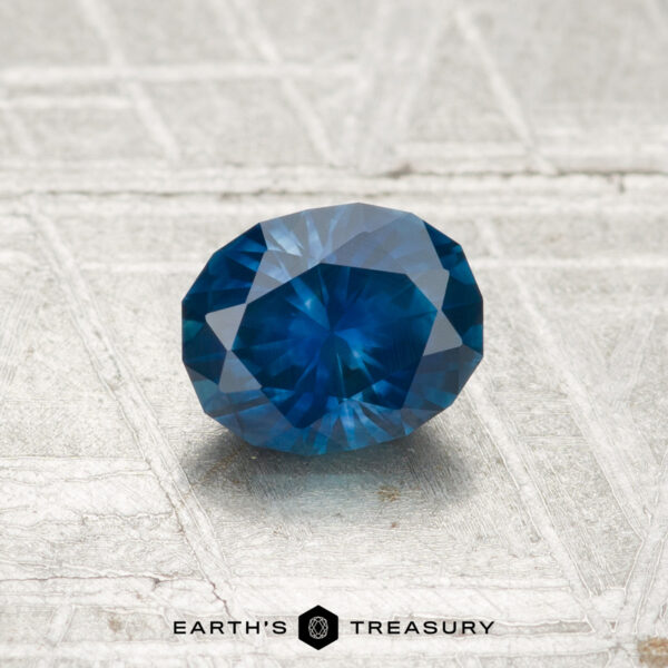 0.80-Carat Montana Sapphire (Heated) A 0.80-carat heated Montana sapphire, faceted in an oval shape, is displayed on a textured light background with the "EARTH'S TREASURY" text and logo beneath it.