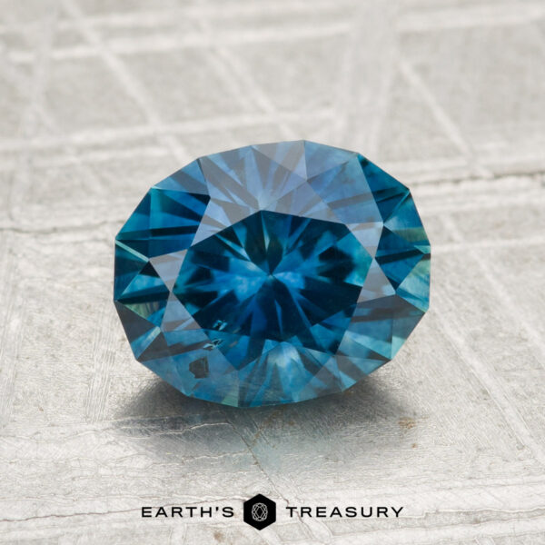 2.08-Carat Montana Sapphire (Heated) A 2.08-carat heated Montana sapphire, cut in a faceted oval shape, is shown on a textured gray surface with "EARTH'S TREASURY" displayed below.