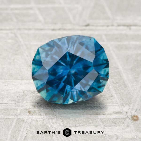 1.75-Carat Montana Sapphire (Heated) A 1.75-carat heated Montana sapphire gemstone is displayed on a textured pale surface with "EARTH'S TREASURY" printed below.