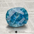 A 3.22-carat heated Montana sapphire is showcased on a textured light surface with "EARTH'S TREASURY" displayed beneath it.