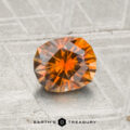 A 1.09-carat heated Montana sapphire with geometric facets rests on a textured, silver-gray surface. "EARTH'S TREASURY" is printed at the bottom of the image.