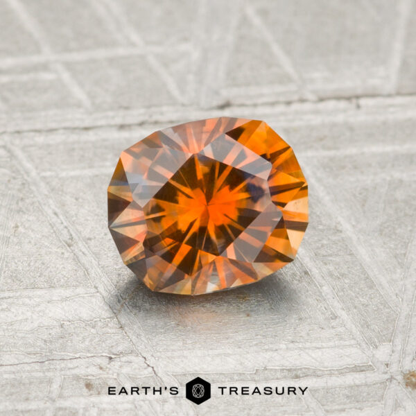 1.09-Carat Montana Sapphire (Heated) A 1.09-carat heated Montana sapphire with geometric facets rests on a textured, silver-gray surface. "EARTH'S TREASURY" is printed at the bottom of the image.