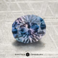 A 2.18-carat heated Montana sapphire with blue and purple hues, cut in a faceted oval shape, rests on a textured surface. "Earth's Treasury" is visible at the bottom of the image.