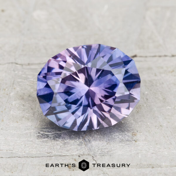 2.18-Carat Montana Sapphire (Heated) 2.18-carat Montana sapphire (heated) with a blue and purple color gradient, faceted oval, displayed on a light textured surface; "Earth's Treasury" logo beneath.
