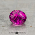 A 1.33-carat heated sapphire, faceted in an oval shape and displaying a pink hue, rests on a textured gray surface with "EARTH'S TREASURY" below it.