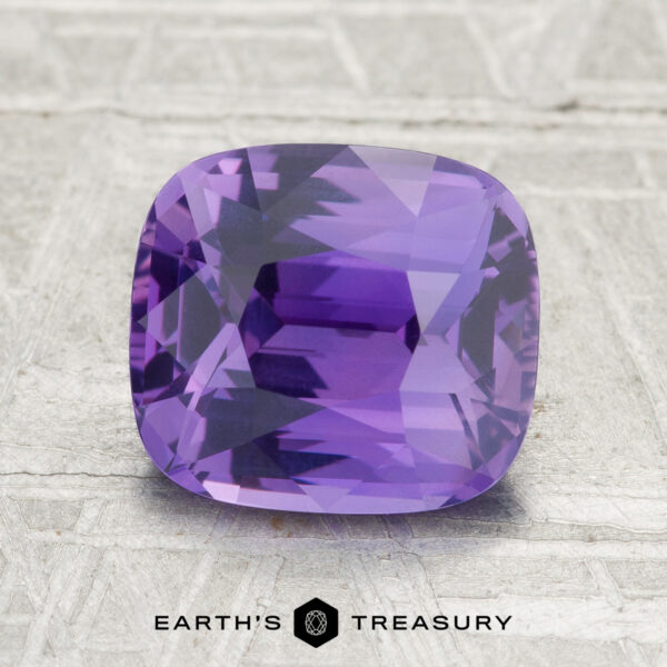 A 3.06-carat Ceylon sapphire with a cushion cut is shown on a textured gray surface, featuring the text "Earth's Treasury" at the bottom.
