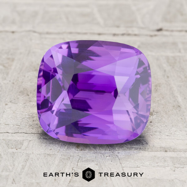 3.06-Carat Ceylon Sapphire A 3.06-carat rectangular cushion-cut Ceylon Sapphire with a pinkish purple hue rests on a textured light surface, with the "EARTH'S TREASURY" text and logo displayed below the stone.