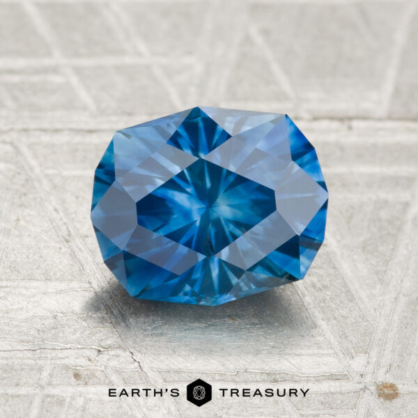1.93-Carat Montana Sapphire (Heated) A 1.93-carat heated Montana sapphire, faceted in an octagonal shape and blue in color, rests on a light-textured surface with "EARTH'S TREASURY" displayed below.