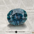 A 2.01-carat oval-cut heated Montana sapphire is displayed on a textured gray surface with "EARTH'S TREASURY" beneath it.