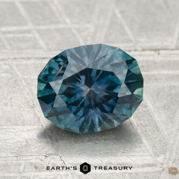 2.01-Carat Montana Sapphire (Heated) A 2.01-carat oval-cut heated Montana sapphire is displayed on a textured gray surface with "EARTH'S TREASURY" beneath it.