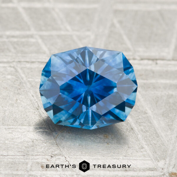 1.85-Carat Montana Sapphire (Heated) A 1.85-carat heated Montana sapphire with an octagonal cut rests on a textured light gray surface. "Earth's Treasury" is displayed at the bottom.