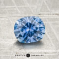 A 1.39-carat heated Montana sapphire is showcased on a textured, light gray surface with "EARTH'S TREASURY" below.