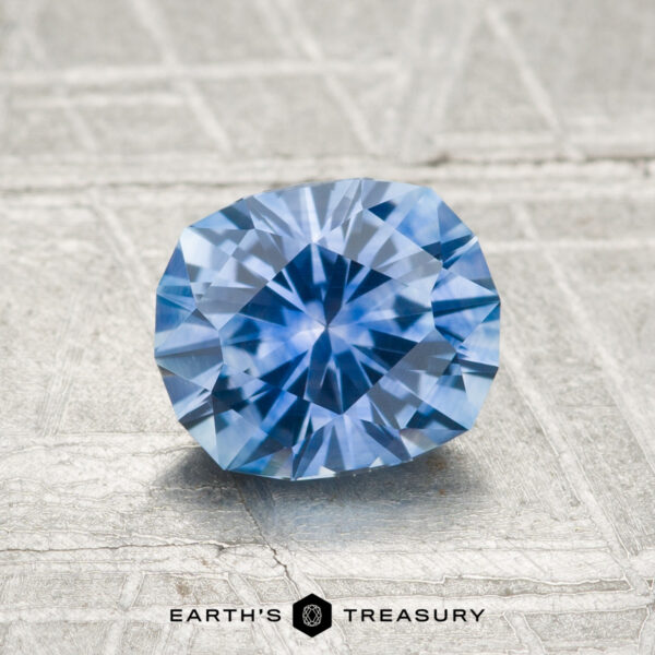 1.39-Carat Montana Sapphire (Heated) A 1.39-carat heated Montana sapphire is showcased on a textured, light gray surface with "EARTH'S TREASURY" below.
