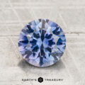 A 2.26-carat heated Montana Sapphire with a round brilliant cut and bluish-purple hue is displayed on a textured light gray surface, featuring "Earth's Treasury" branding at the bottom.