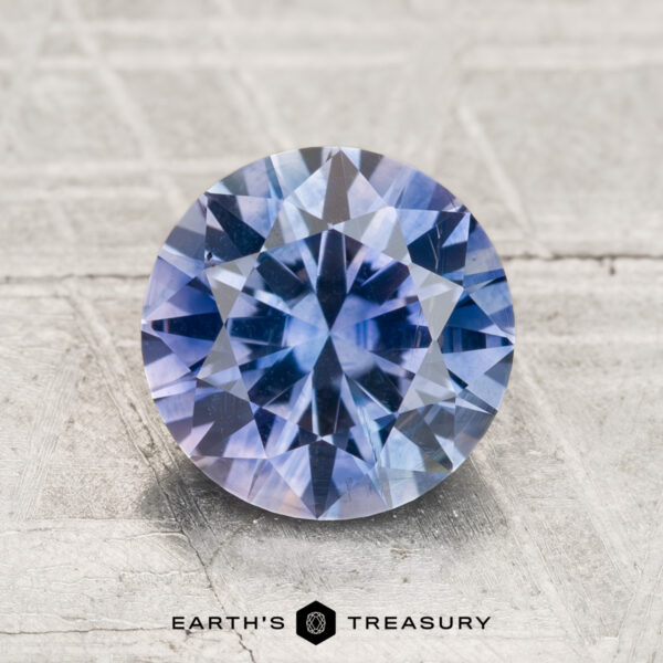 2.26-Carat Montana Sapphire (Heated) A 2.26-carat heated Montana Sapphire with a round brilliant cut and bluish-purple hue is displayed on a textured light gray surface, featuring "Earth's Treasury" branding at the bottom.