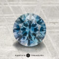 A 2.26-carat heated Montana sapphire, cut in a round brilliant style, sits on a textured light gray surface with "EARTH'S TREASURY" displayed at the bottom.