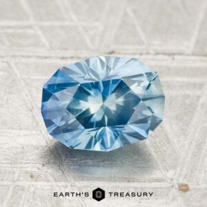 A 2.18-carat heated Montana sapphire is displayed on a textured surface with the text "Earth's Treasury" below.