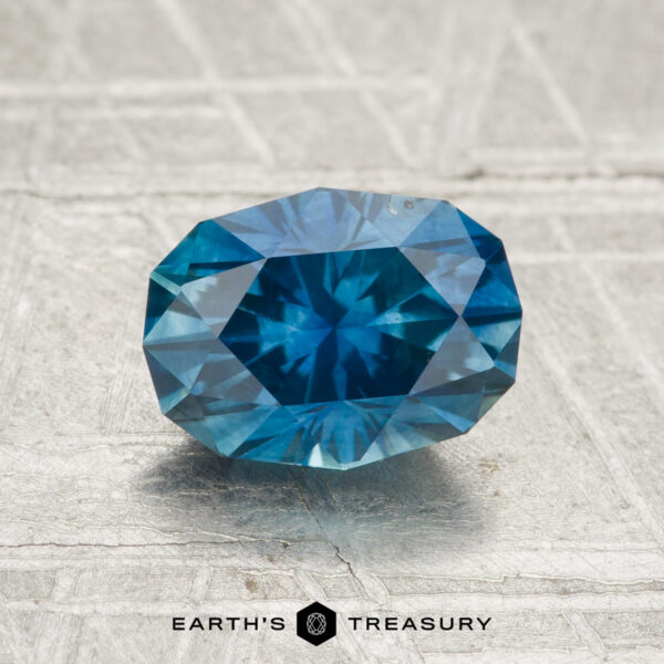 1.76-Carat Montana Sapphire (Heated) A 1.76-carat heated Montana sapphire is displayed on a textured surface with the "Earth's Treasury" logo beneath it.