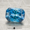 A 2.80-carat heated Montana sapphire, rectangular and faceted, rests on a light textured surface with "Earth's Treasury" and logo below.