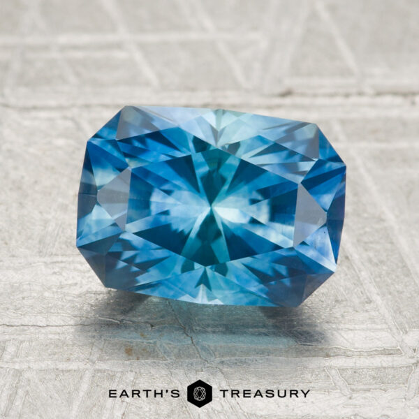 2.80-Carat Montana Sapphire (Heated) A 2.80-carat heated Montana sapphire, rectangular and faceted, rests on a light textured surface with "Earth's Treasury" and logo below.