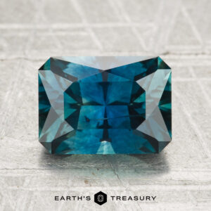A 2.88-carat heated Montana sapphire with a rectangular, teal-blue faceted cut displayed on a textured surface and the "Earth's Treasury" logo below.