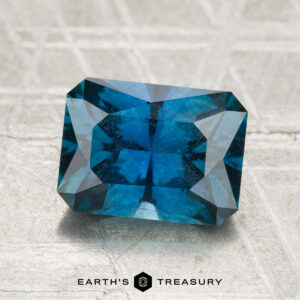 A 2.68-carat heated Montana sapphire, cut in a rectangular shape, is displayed on a textured light surface with the Earth's Treasury logo at the bottom.