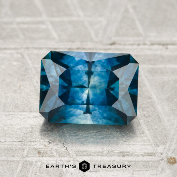 1.88-Carat Montana Sapphire (Heated) A 1.88-carat heated Montana sapphire, cut in a rectangular faceted shape, rests on a textured metallic surface with the Earth’s Treasury logo below.