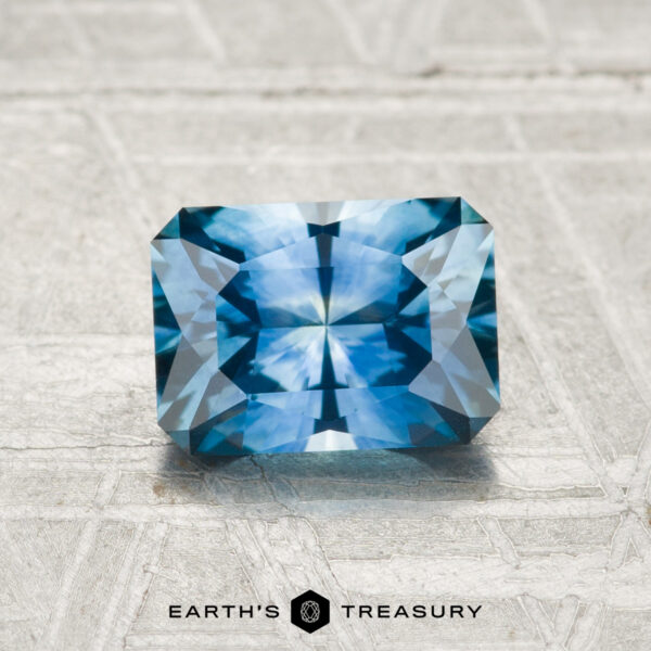 1.35-Carat Montana Sapphire (Heated) A 1.35-carat rectangular, faceted Montana Sapphire (heated) is displayed on a light textured surface with the text "EARTH'S TREASURY" below it.