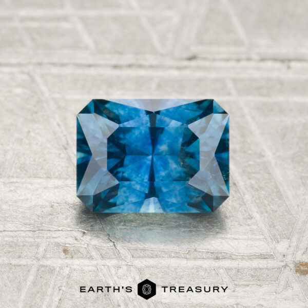 1.22-Carat Montana Sapphire (Heated) A 1.22-carat heated Montana sapphire, cut in a rectangular shape with multiple facets, rests on a textured light surface with "EARTH'S TREASURY" written below.
