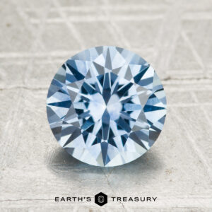 A 2.40-carat heated Montana sapphire in round brilliant cut is shown on a textured light surface with the Earth’s Treasury logo below.