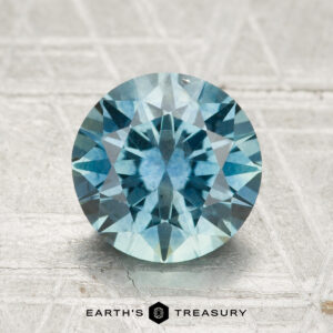 2.36-carat heated Montana sapphire, round and blue with faceted cut, displayed on a light textured surface featuring the "Earth's Treasury" logo below.