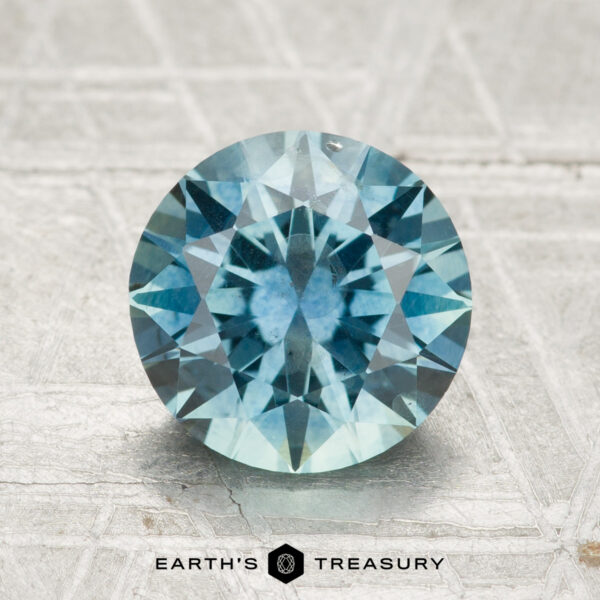 2.36-Carat Montana Sapphire (Heated) 2.36-carat heated Montana sapphire, round and blue with faceted cut, displayed on a light textured surface featuring the "Earth's Treasury" logo below.