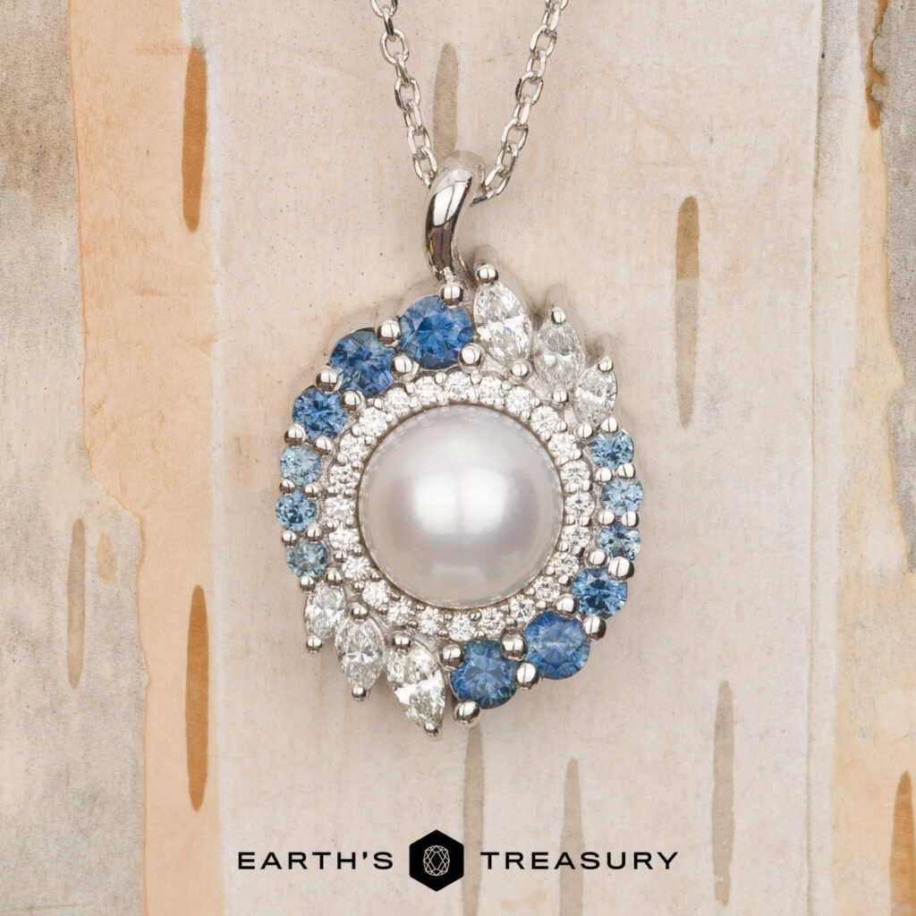 A silver pendant necklace with a central round pearl, blue and clear gemstones sits on a light patterned background. The "Sanders, Brandon and Kerri 5 [custom gallery]" logo is displayed below.