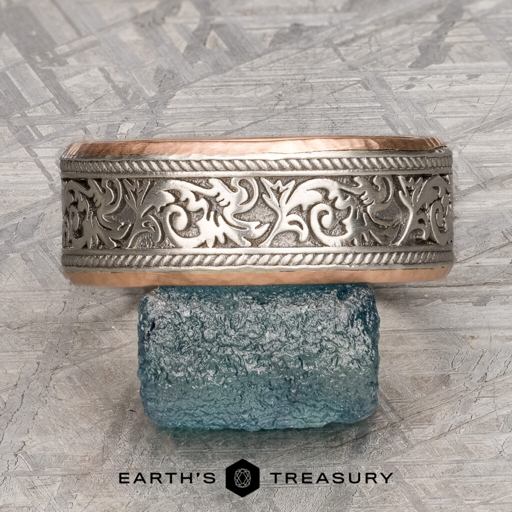 The "Vaughan, Maggie and Ryan 4 [custom gallery]" ring, featuring a silver and rose gold pattern, is displayed on a rough blue gemstone with the Earth's Treasury logo beneath.