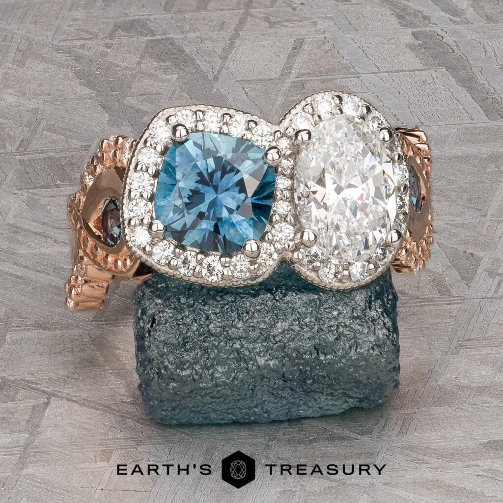 Two gemstone rings from "Acosta, Tracy 2 [custom gallery]"—one featuring a blue stone, the other a clear stone, both encircled by small diamonds—are displayed on a rough mineral with the "Earth's Treasury" logo below.
