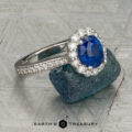 The "Josephine" ring in 18K white gold, featuring a 1.60-carat Ceylon sapphire with a prong-set halo of diamonds, is displayed on a blue-green gemstone against a patterned gray background with the "Earth's Treasury" logo below.