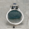 The "Josephine" ring in 18K white gold, featuring a 1.60-carat Ceylon sapphire with a prong-set halo of diamonds, is displayed on a blue-green gemstone against a patterned gray background with the "Earth's Treasury" logo below.