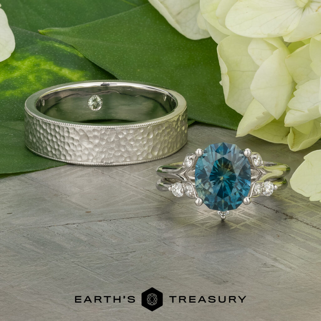 The "Stacked from 59 images. Method=B (R=14,S=1)" features two rings on wood with leaves and white flowers: one is a hammered metal band, the other a gemstone ring set with a blue oval stone and diamond accents.