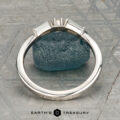 The "Narelle" band in 18K white gold, featuring a round center diamond and two tapered baguette diamonds, is displayed on a rough blue gemstone with the "Earth's Treasury" logo below.