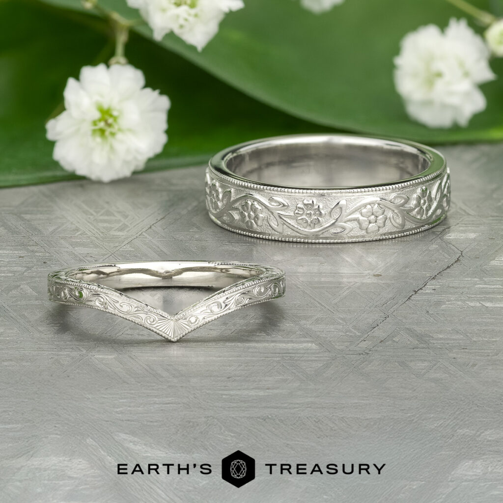 Two ornate silver rings with engraved floral patterns are displayed on a textured surface, white flowers and green leaves behind them. The logo "EARTH'S TREASURY" appears below. Product shown: Stacked from 42 images. Method=B (R=14,S=2).