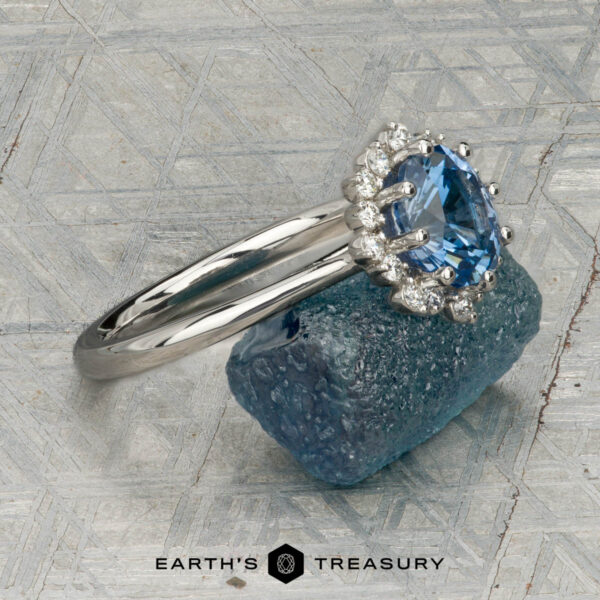 Custom ring in platinum with 1.27-carat Montana sapphire The "Celisse" ring in platinum, featuring a 1.27-carat Montana sapphire, is displayed on a rough blue mineral, with the "Earth's Treasury" logo below.