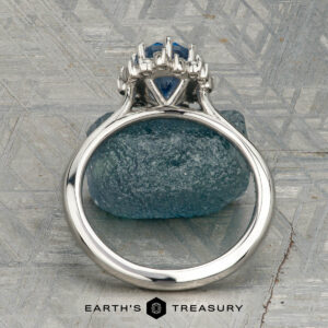 The "Celisse" ring in platinum, featuring a 1.27-carat Montana sapphire, is displayed on a rough blue mineral, with the "Earth's Treasury" logo below.