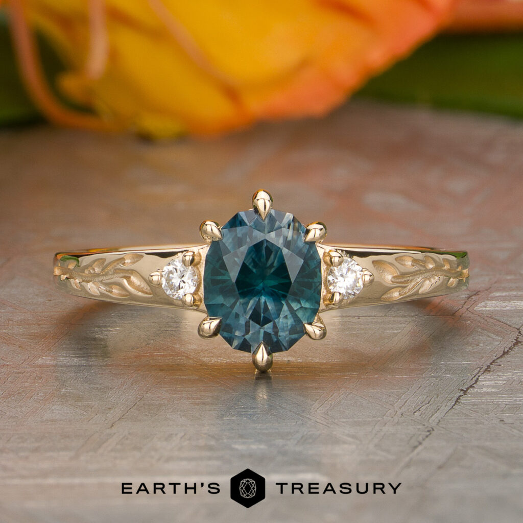 The Rahal-Arabi, Nour ring features an oval blue gemstone center with two small round diamonds, displayed on a metallic surface above the text "Earth's Treasury.