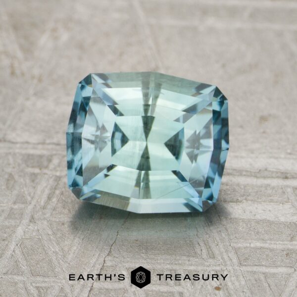 2.15-Carat Montana Sapphire A rectangular, faceted blue-green 2.15-carat Montana Sapphire rests on a textured surface featuring the "Earth's Treasury" logo and text below it.