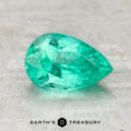 A 1.15-carat pear-shaped, faceted Colombia emerald (oiled) rests on a light textured surface with the text "EARTH'S TREASURY" below.