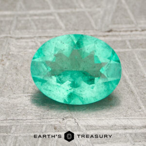 A 1.17-carat Colombia emerald (oiled), oval-cut and green, rests on a textured gray surface with the Earth's Treasury logo below.