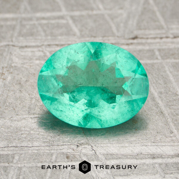 1.17-Carat Colombia Emerald (Oiled) A 1.17-carat Colombia emerald (oiled), oval-cut and green, rests on a textured gray surface with the Earth's Treasury logo below.